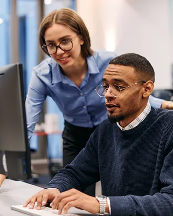 Man sitting, woman standing next to him, they are both looking at a computer screen