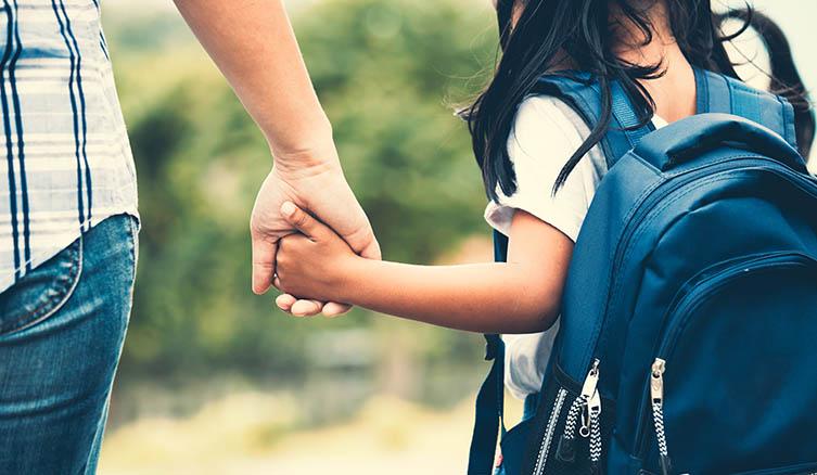 Girl with backpack holding a parent's hand