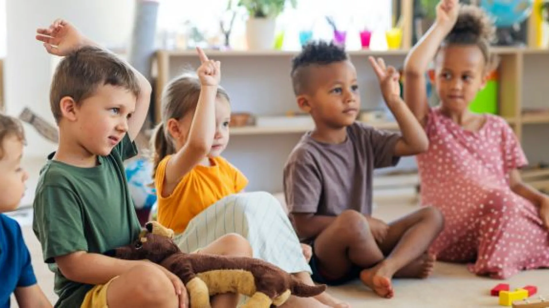 Preschool children seated in a circle raising hands