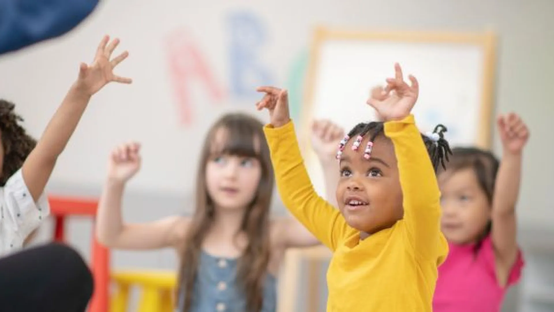 Preschool children seated in a circle raising hands