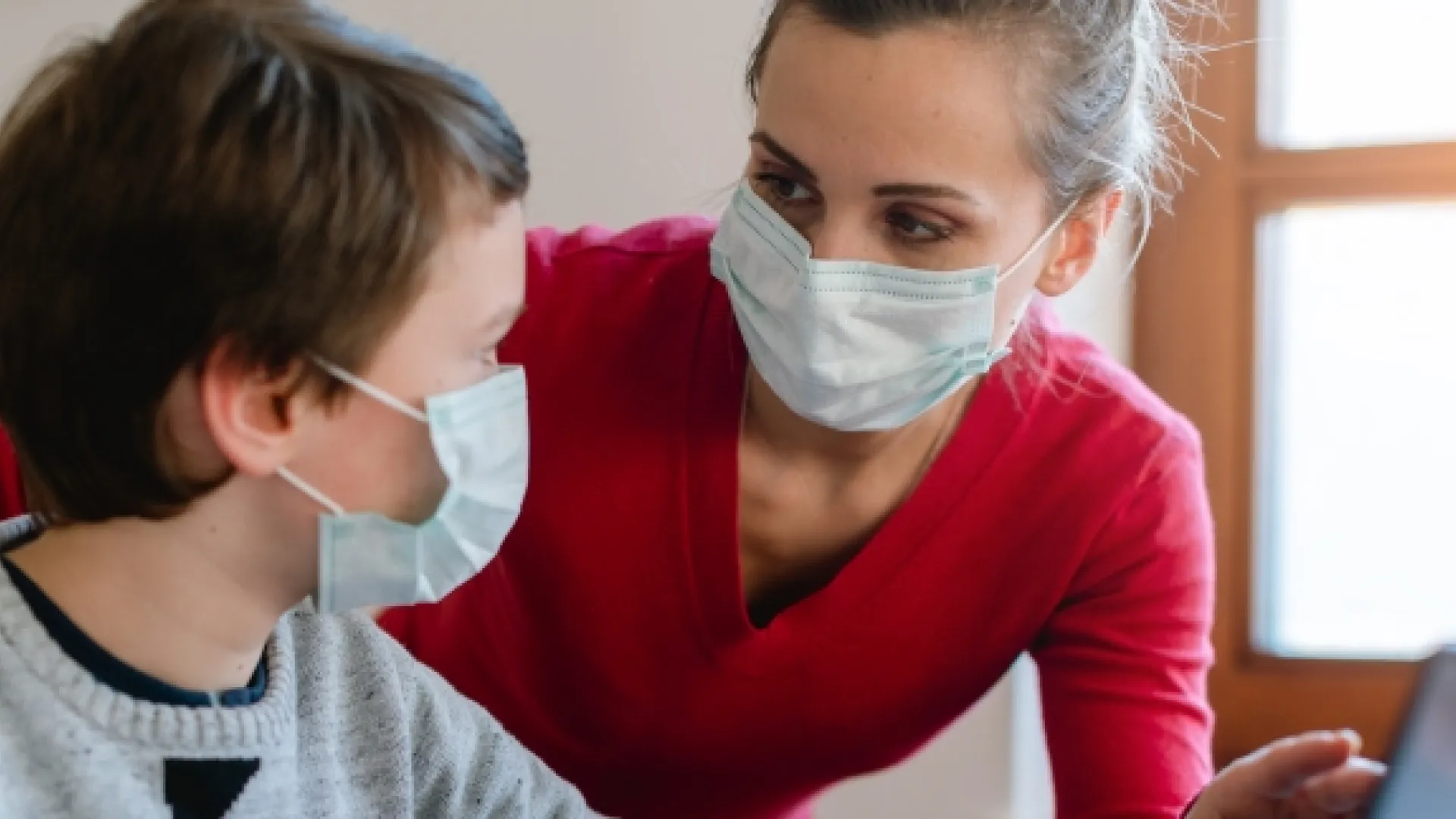 teacher and student wearing masks and talking while looking at a laptop
