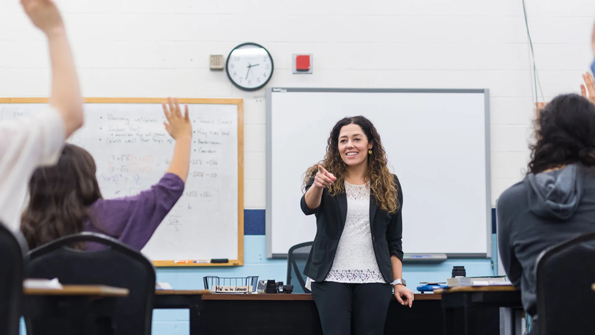 Teacher standing at front of classroom with students hands raised