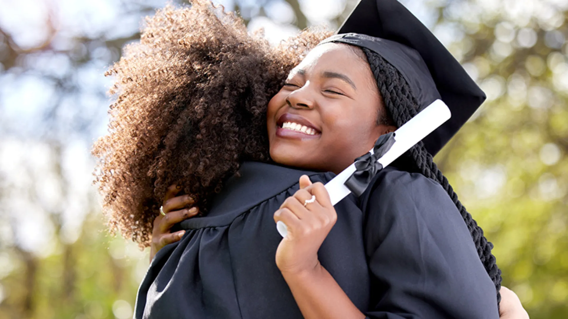 graduate hugging friend and holding diploma
