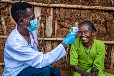 Male doctor taking senior woman temperature in remote village, East Africa 