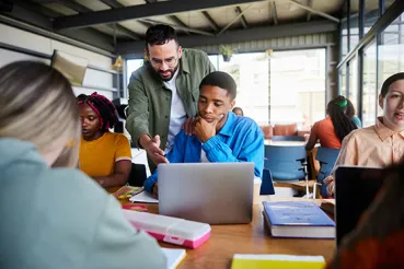 Trainer helping student on laptop in classroom