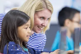 teacher and young student working closely on laptop