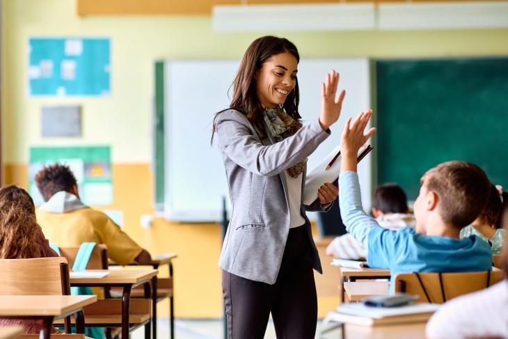 Happy elementary school teacher giving high-five to her student during class in the classroom