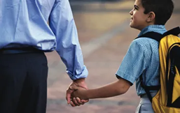 Image of boy with backpack holding his father's hand