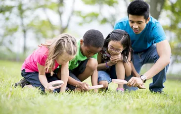 Image of young teacher with students using magnifying glasses outside