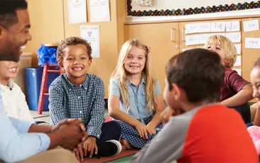 Children with teacher sitting on classroom floor and smiling