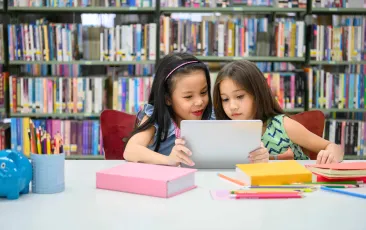 Two girls in a library looking at a tablet