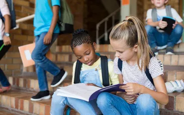 Two girls reading together on school steps