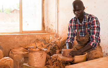 Concentrated African craftsman enjoying work with clay on potter wheel, making ceramic dishes