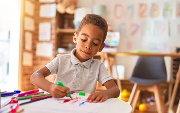 African American kindergartner drawing at school table