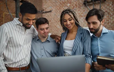 Cheerful young businesspeople with laptop working in office, social inclusion and cooperation