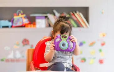 little girl holding up a toy camera in a classroom
