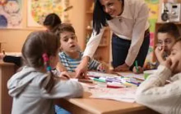 Happy preschool teacher assisting children with their drawings