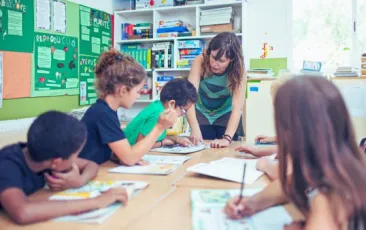 female teacher working at a table with four elementary students