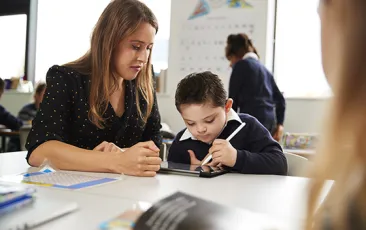 female teacher working with young student on tablet