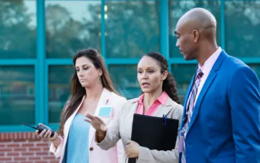 three principals talking outside a school