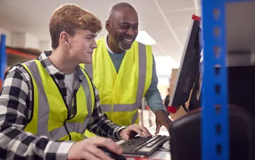 intern and supervisor working on computer in warehouse