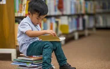 Little boy sitting on books in library