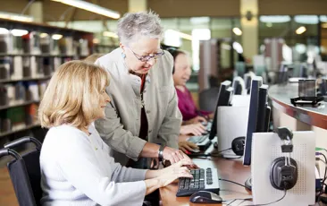 Older library volunteer helping patron