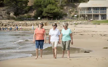 Three older women walking on a beach
