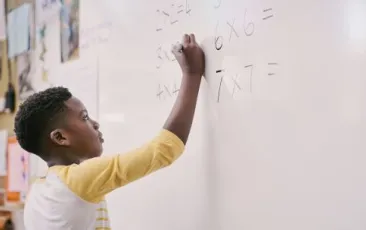 Student working on math problem on whiteboard.