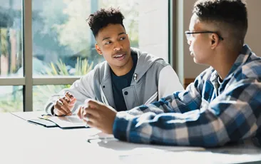 Two high school students talking in library