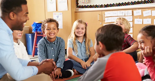 Children with teacher sitting on classroom floor and smiling