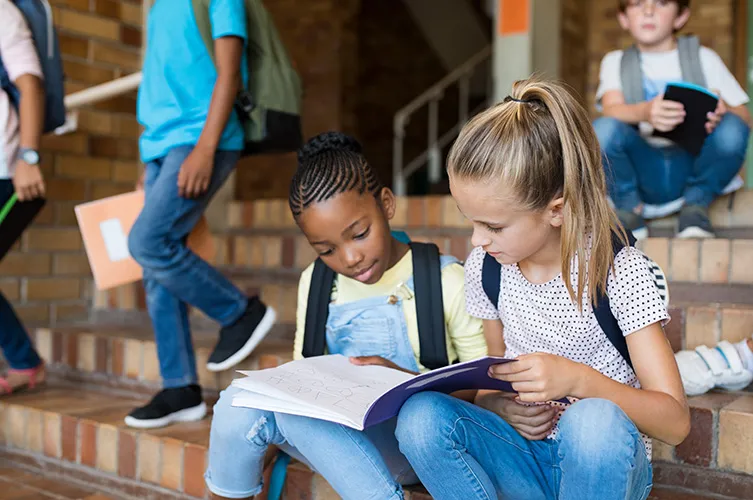 Two girls reading together on school steps