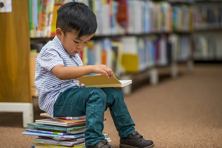 Little boy sitting on books in library