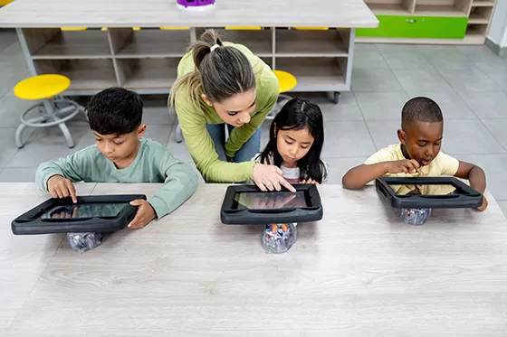 Teacher helping young students on iPads