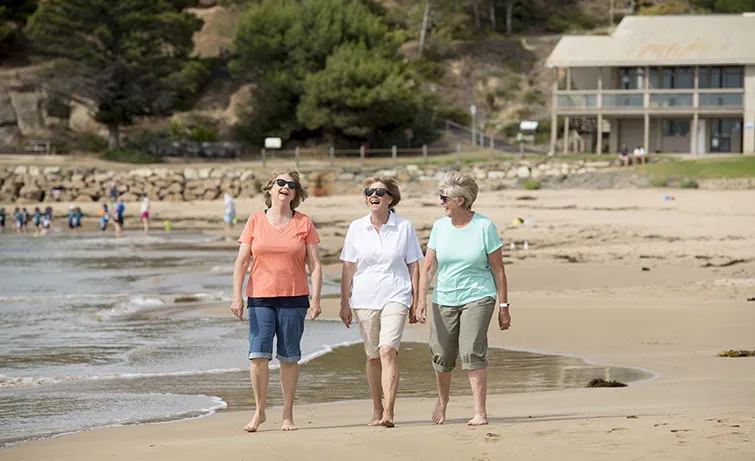 Three older women walking on a beach