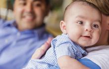 Image of baby in a gingham shirt being held by a parent 
