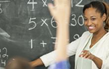 Image of teacher at chalkboard smiling at student raising hand