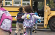 Diverse group of children running towards a school bus