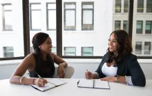 Two women chatting in front of an office window