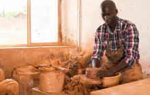 Concentrated African craftsman enjoying work with clay on potter wheel, making ceramic dishes
