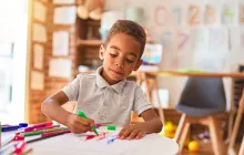 African American kindergartner drawing at school table