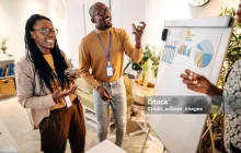 Three people discussing graphs on a board. 
