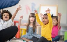 Preschool children seated in a circle raising hands