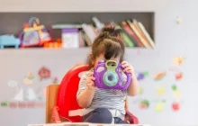 little girl holding up a toy camera in a classroom