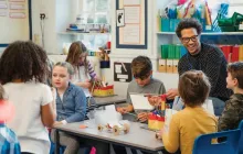Teacher smiling and talking at tables with elementary students