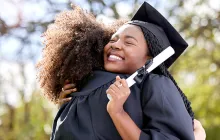 graduate hugging friend and holding diploma
