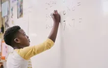 Student working on math problem on whiteboard.