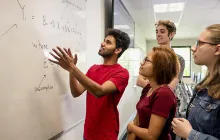 College students working a math problem at a whiteboard